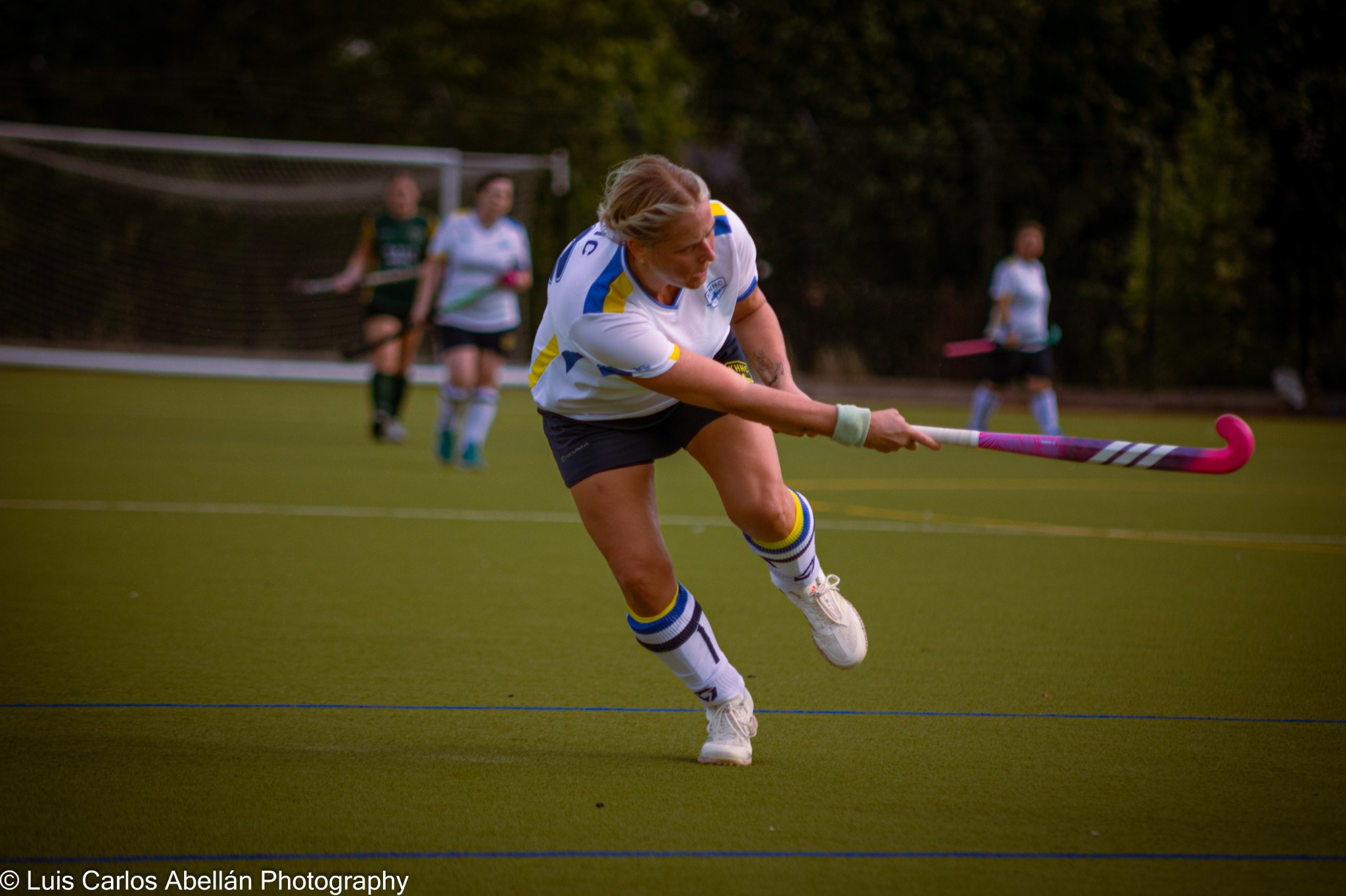 Player in white strikes the hockey ball with a pink stick.