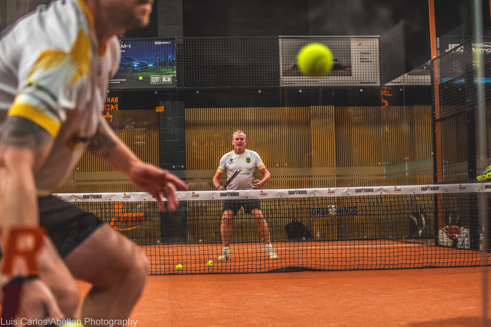 Padel doubles players face each other across the net as the ball crosses the court.