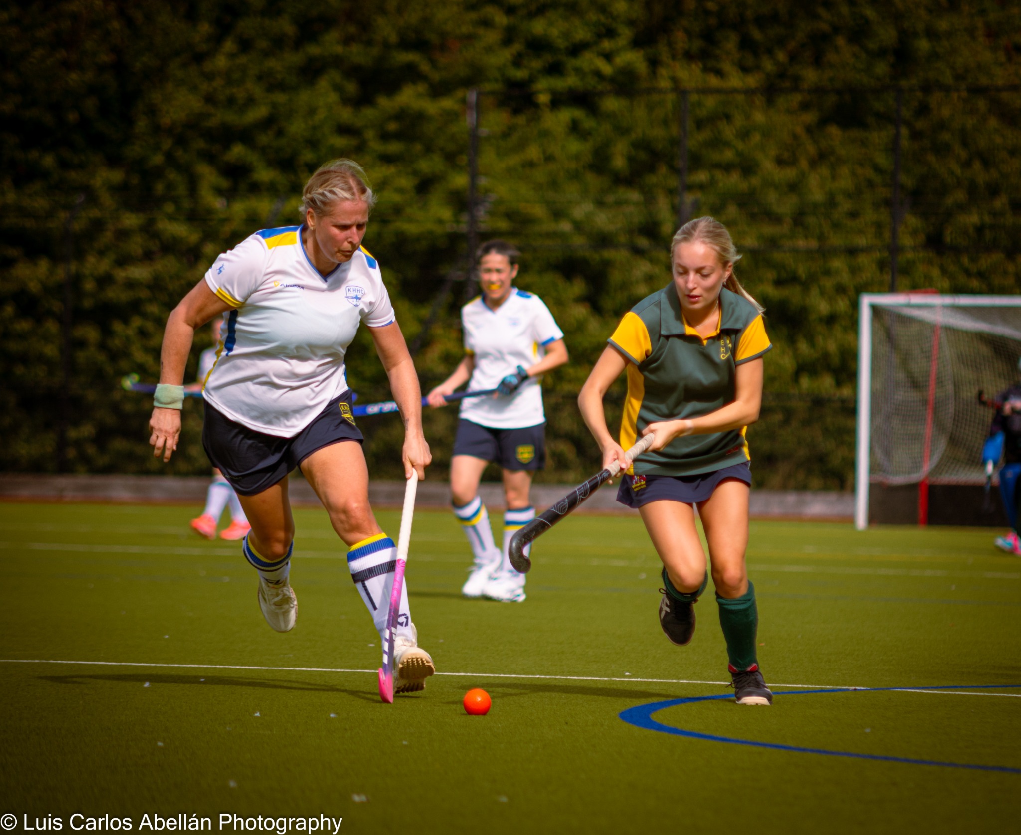 Hockey players in white and green contesting the ball on the pitch