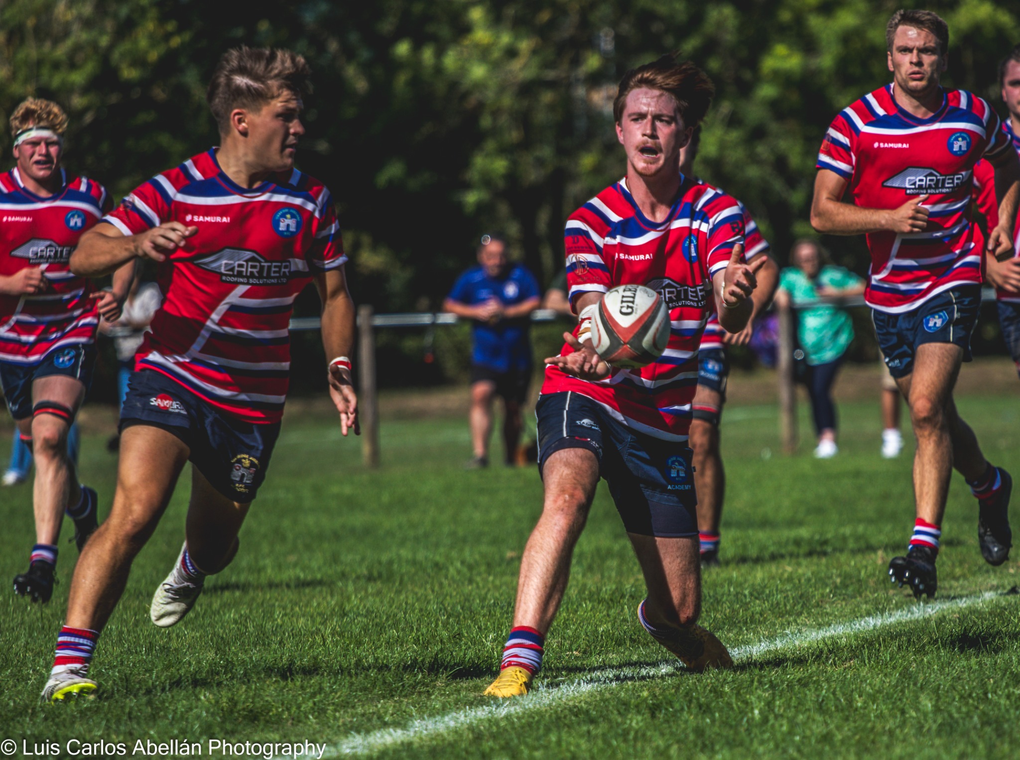 Rugby players in red and blue stripes moving forward with the ball