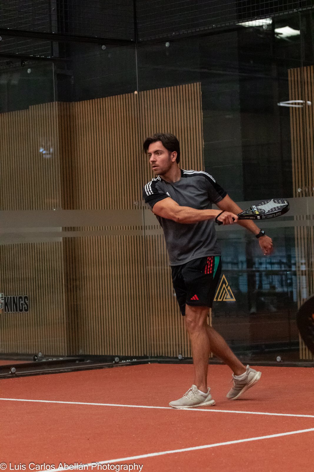 Padel player prepares a shot on an indoor court.