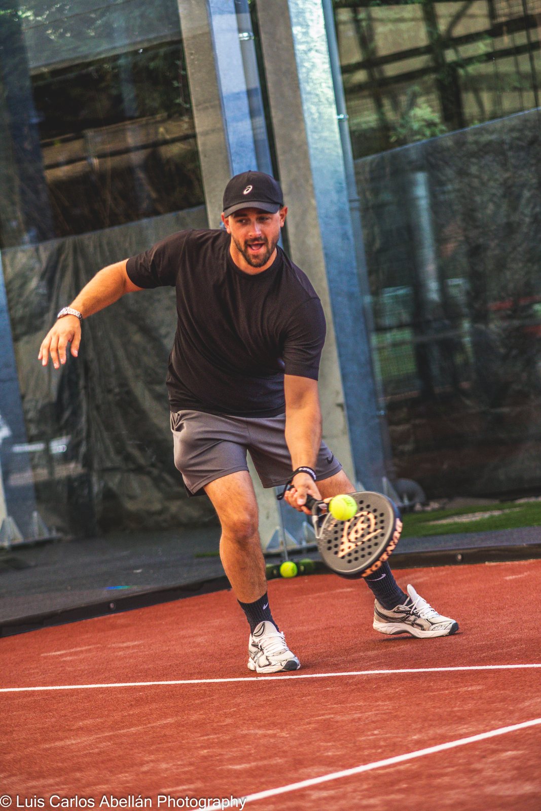 Padel player stretches to meet the ball on an outdoor court.