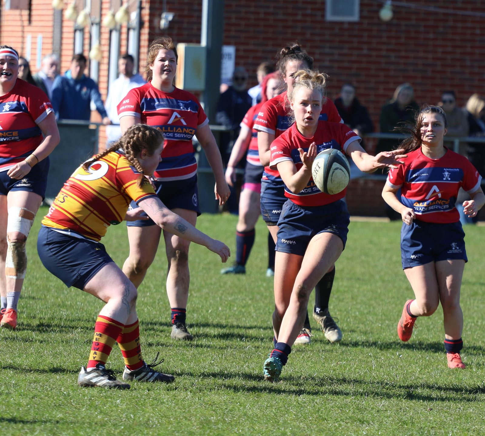 Women rugby players chase a ball carrier during open play.
